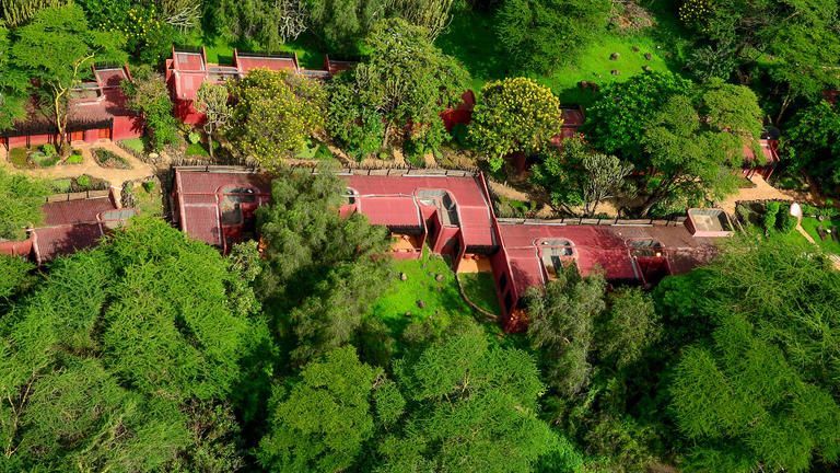 Amboseli Serena Safari Lodge Aerial View - Nestled in the foothills of the snow-capped 6,000-meter Mount Kilimanjaro and surrounded by giant acacia trees and a gently flowing natural spring, this magnificent Safari Lodge awaits. Inspired by Maasai architecture, the guest rooms are adorned with authentic Maasai beadwork and African murals, blending seamlessly with the natural environment.